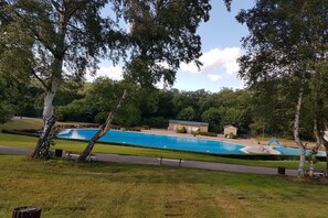 A swimming pool with a clear blue water feature, surrounded by trees and a grassy area. - Holiday apartment with 2 bedrooms (Thale\/OT Altenbrak)