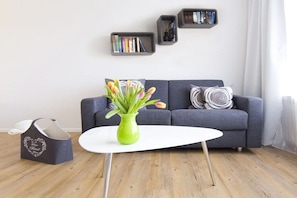 A modern living room with a grey sofa, a white coffee table, a green vase with flowers, and bookshelves on the wall. - Mati's panoramic view (Meersburg)