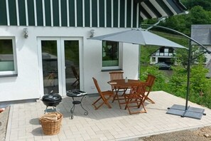 An outdoor patio with a table and chairs, a grill, and a covered area. - Holiday home with 2 bedrooms (Lennestadt-Milchenbach)