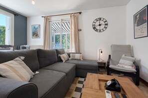 A modern living room with a grey sectional sofa, a wooden coffee table, a side table with a lamp, and a wall clock. - Holiday Home 'Chez Négus' with Wi-Fi and Air Conditioning (Laruns)
