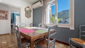 A dining area with a wooden table and chairs, a mirror, and a window with a view of houses and hills.