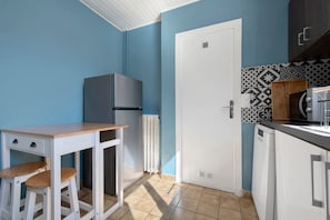 A compact kitchen with a white refrigerator, a wooden table with stools, a white door, and patterned backsplash tiles. - Holiday Home 'Chez Négus' with Wi-Fi and Air Conditioning (Laruns)