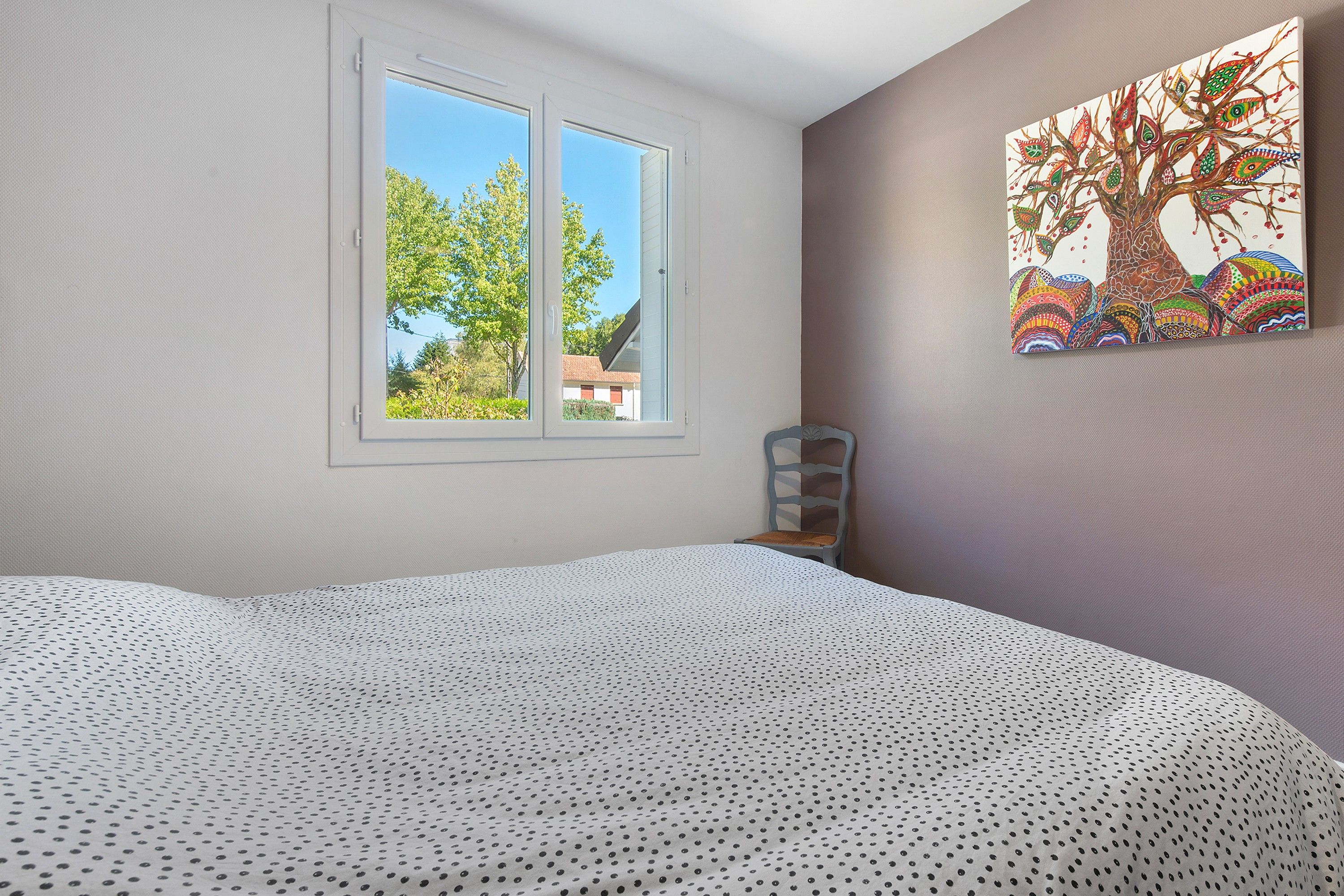 A bedroom with a bed, a window, and a wall-mounted painting.