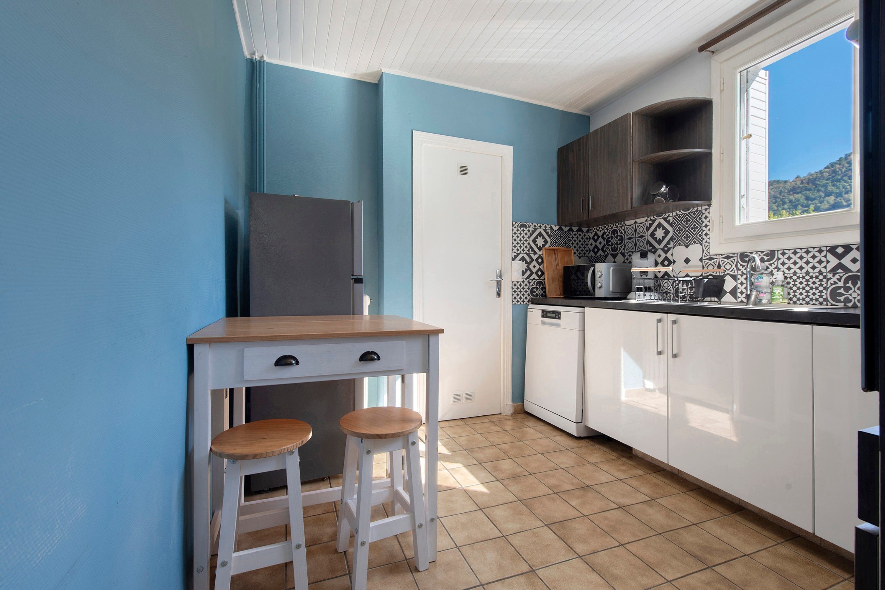 A compact kitchen with a single refrigerator, a sink, a stove, and a window with a view of the outdoors.