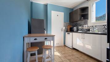 A compact kitchen with a single refrigerator, a sink, a stove, and a window with a view of the outdoors.