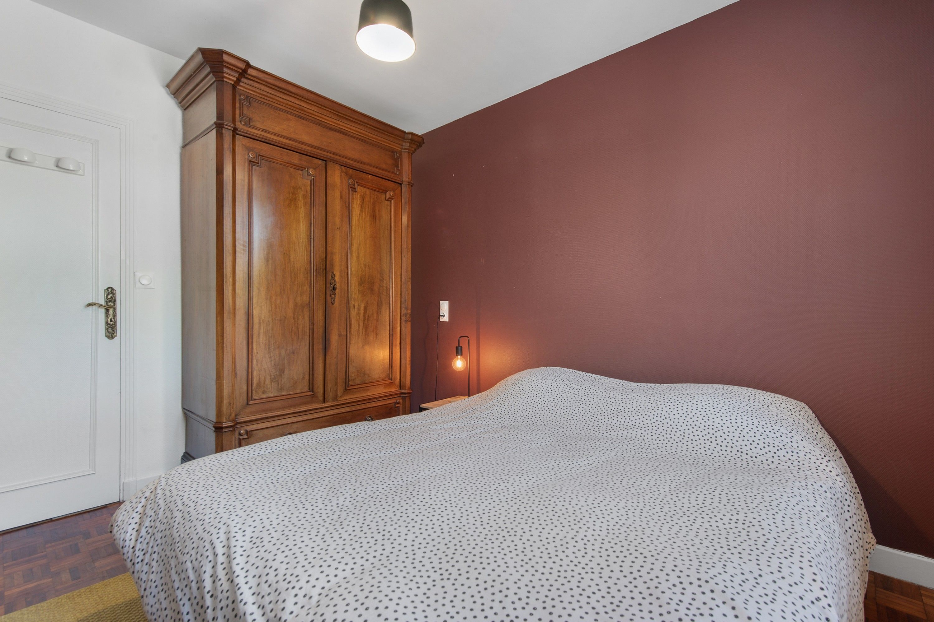 A bedroom with a bed, a wardrobe, a door, and a wall-mounted light fixture.