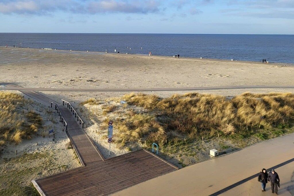 A beach with a wooden boardwalk leading to the water, a sandy area, and a clear sky.