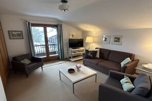 A living room with a sofa, armchairs, a coffee table, a TV, and a balcony with curtains. - Holiday apartment with 1 bedroom (Reit im Winkl)