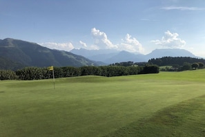 A golf course with a flagstick, surrounded by mountains and clear skies. - Holiday apartment with 1 bedroom (Reit im Winkl)