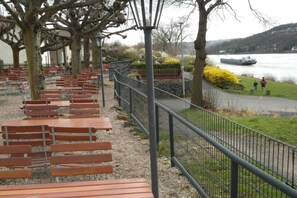 Ein Park am Flussufer mit Holzbanken, einem Metallzaun und einem Boot auf dem Wasser.
