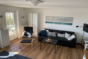 Ein Wohnzimmer mit einem schwarzen Sofa, einem Couchtisch, einem Sessel, einem Schrank und Kunstwerken an der Wand.