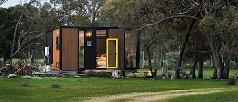 A modern, compact cabin with a visible bedroom and a small outdoor seating area.