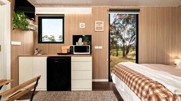A modern bedroom with a bed, a small kitchenette, and a view of the outdoors.
