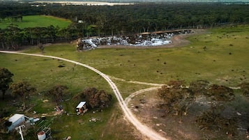 An aerial view of a rural property with a dirt road, a small building, and a fenced area.