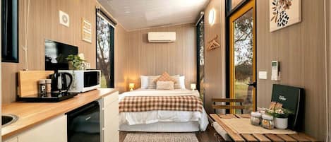 A compact room with a bed, bedside table, and a small kitchenette area.