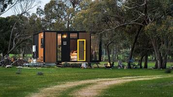 A modern, compact cabin with a visible bedroom and a small outdoor seating area.