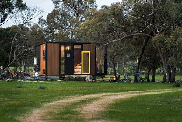A modern, compact cabin with a visible bedroom and a small outdoor seating area.