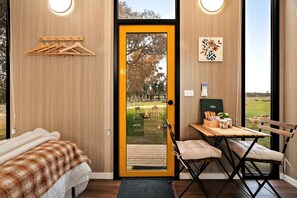 A room with a bed, a chair, a table, and a door leading to an outdoor area.
