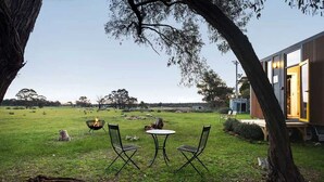 Uma área de estar externa com mesa, cadeiras, lareira e um edifício com porta aberta.