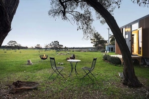 Un espacio al aire libre con mesa y sillas, un brasero y un edificio con puerta abierta.