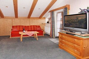 Ein Zimmer mit Holzboden, einem roten Sofa, einem HolztV-Möbel und einem Fernseher, der eine Landschaft zeigt.