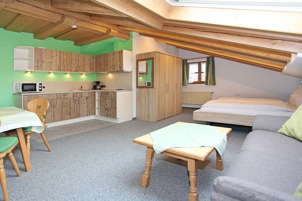 A compact, well-lit room with a kitchenette, a dining area, a sofa, and a bed.