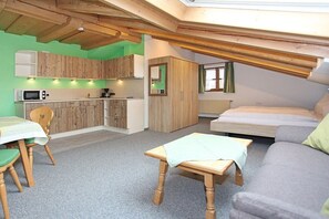 Een compacte, goed verlichte kamer met een kitchenette, een eethoek, een bank en een bed.