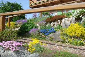 Ein Garten mit verschiedenen Blumen und Pflanzen, einer hölzernen Pergola und einem gepflasterten Weg.