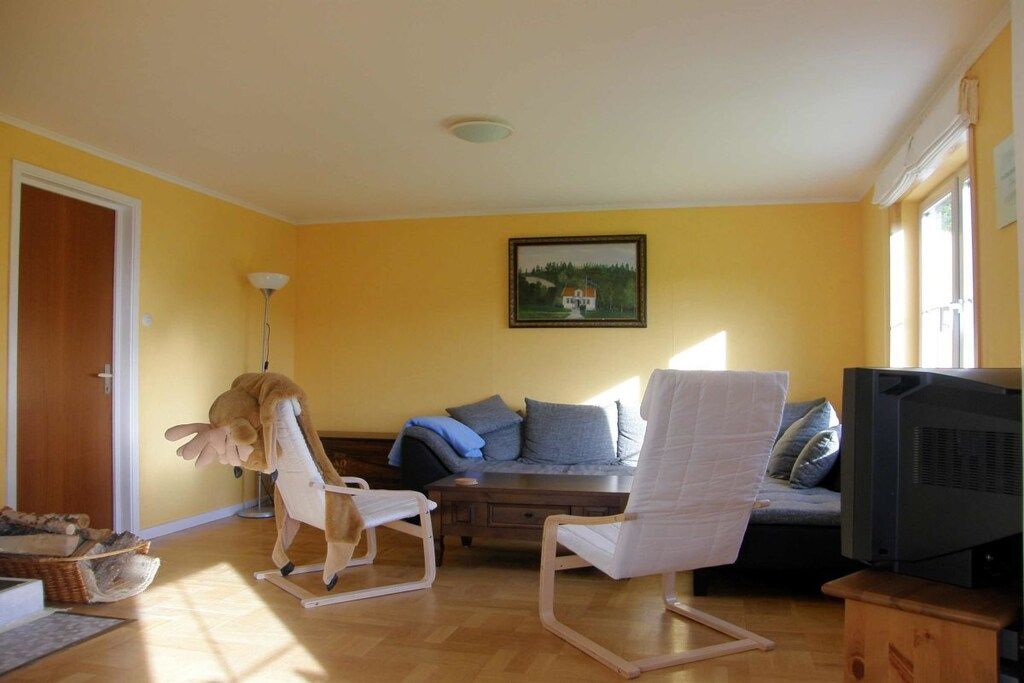 Ein Wohnzimmer mit einer Couch, zwei Sesseln, einem Fernseher und einem Bild an der Wand.