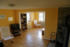 A living room with a fireplace, a television, a bookshelf, and a white chair. - Holiday home in Bullaren with swimming pool (Bullaren)