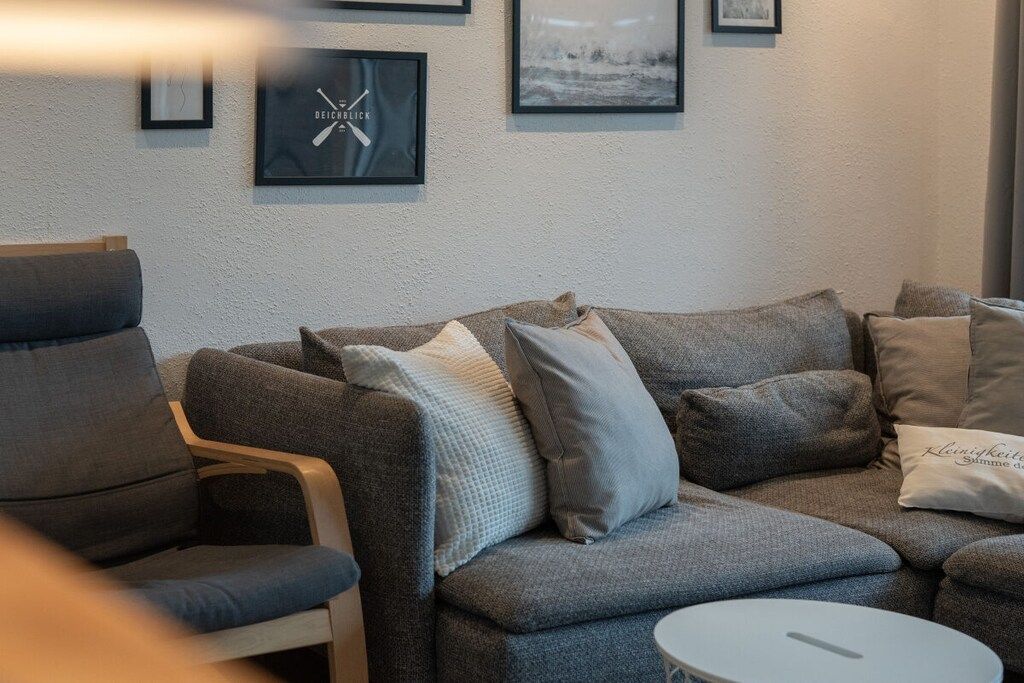 Een moderne woonkamer met een grijze bank, een houten fauteuil en een klein, wit bijzettafeltje.