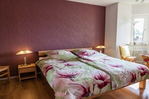 Ein Schlafzimmer mit einem Bett, zwei Nachttischen, einem Sessel und einem Fenster.