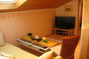 A cozy room with a bed, a small table with decorative items, a television, and a wicker chair. - 3 on the Demelhof || Bernau (Bernau)