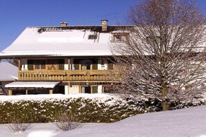 A two-story building with a balcony, surrounded by snow-covered ground and a leafless tree. - Holiday apartment with 2 bedrooms (Altenau)
