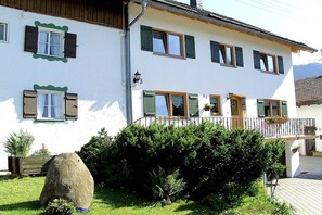 Un bâtiment à deux étages doté d’un balcon, avec une pierre au premier plan et une montagne en arrière-plan.