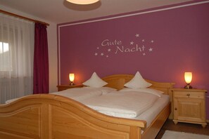 Quarto com cama de madeira, duas luminárias de cabeceira, mesa de cabeceira e parede com desenho de céu estrelado.