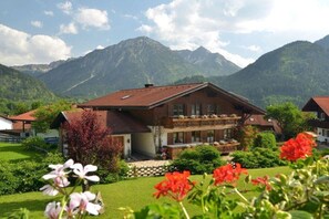 A chalet with a sloped roof, multiple balconies, and a garden with flowers. - Holiday apartment with 1 bedroom (Bad Hindelang)