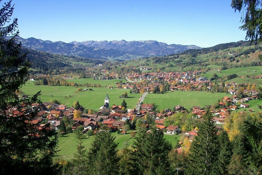 Eine Stadt liegt eingebettet in ein Tal, mit Blick auf eine Kirche und Berge.