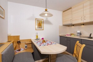 A compact kitchen with a dining area, wooden cabinets, a pendant light, and a framed picture on the wall. - Holiday apartment with 1 bedroom (Bad Hindelang)