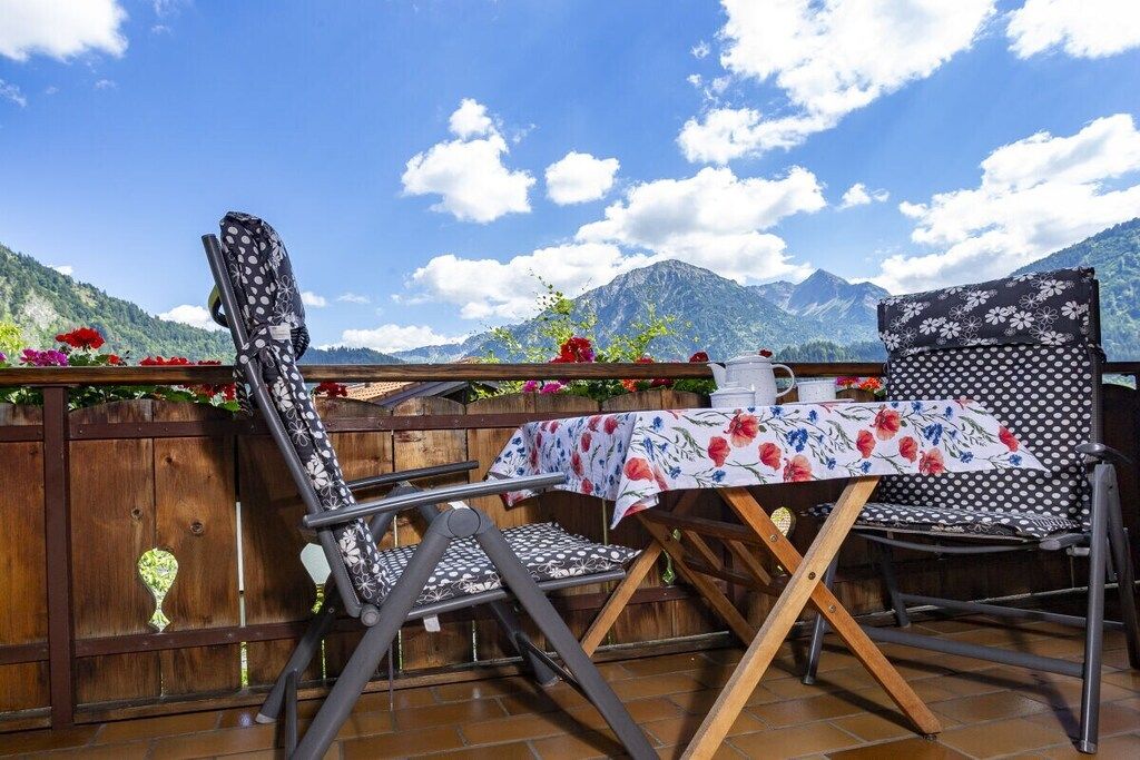 An outdoor seating area with a table and chairs, a wooden fence, and a mountain view.