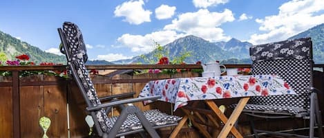 An outdoor seating area with a table and chairs, a wooden fence, and a mountain view.