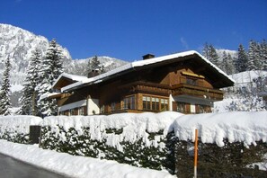 Un hôtel de style chalet, avec une façade en bois, de grandes fenêtres et un toit recouvert de neige.