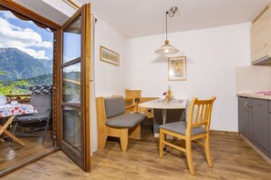 Un coin repas avec une table et des chaises, une fenêtre donnant sur les montagnes et un espace cuisine avec des placards et un luminaire suspendu.