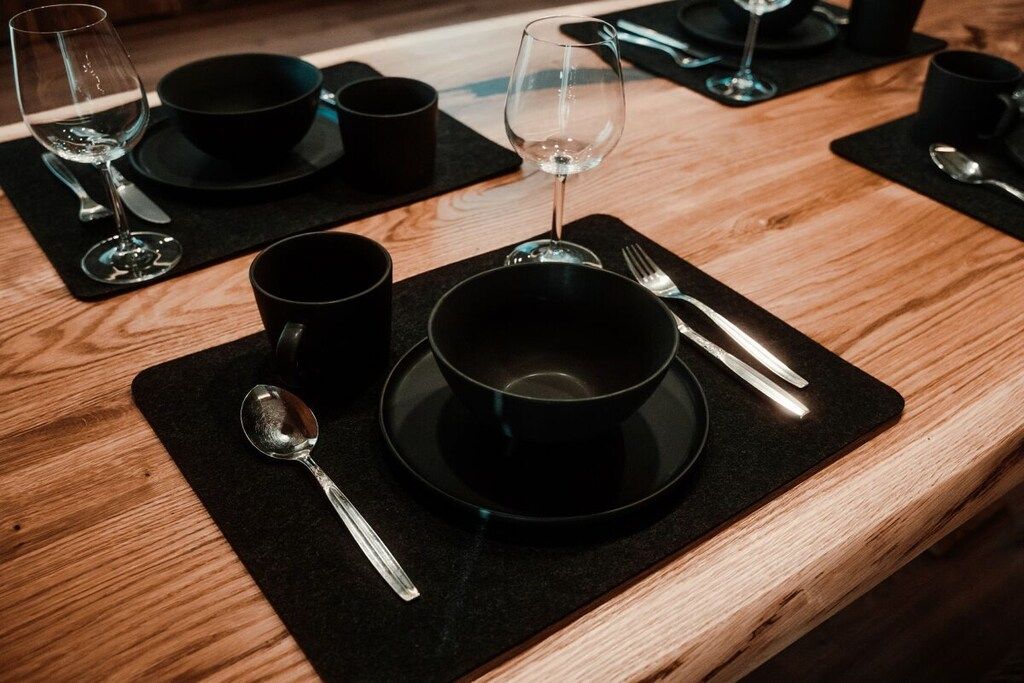 A table set with black placemats, a bowl, a wine glass, and cutlery.