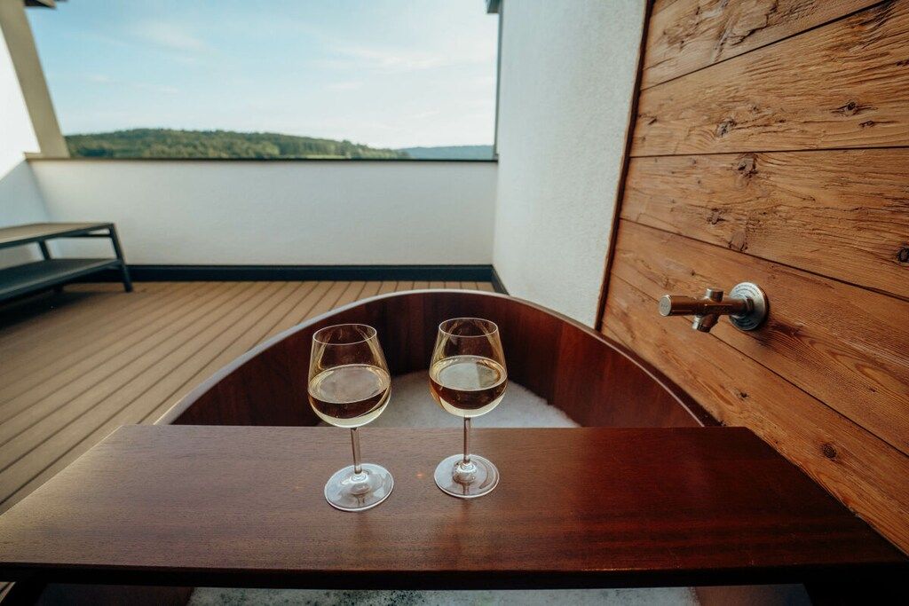 Eine Holzwanne mit zwei Gläsern Weißwein auf einem Balkon mit Blick auf die Landschaft.