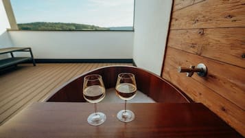 Eine Holzwanne mit zwei Gläsern Weißwein auf einem Balkon mit Blick auf die Landschaft.
