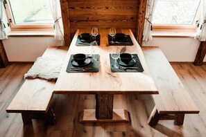 Ein Holztisch mit vier Sätzen schwarzer Schüsseln und Weingläsern, auf einem hellen Holzboden mit einem Fellteppich, in einem Raum mit Holzwänden und einem Fenster.