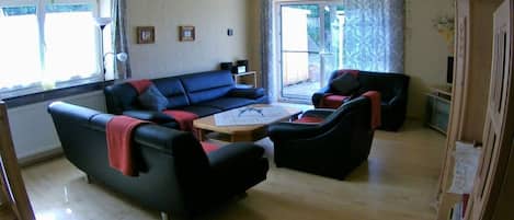 A living room with a sofa set, a coffee table, and a sliding glass door leading to an outdoor area.