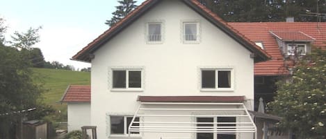A two-story house with a red-tiled roof, white walls, and a small front porch.