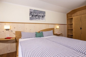 Habitación de hotel con cabecera de madera, ropa de cama a cuadros, mesita de noche con lámpara, fotografía enmarcada en la pared y armario de madera.